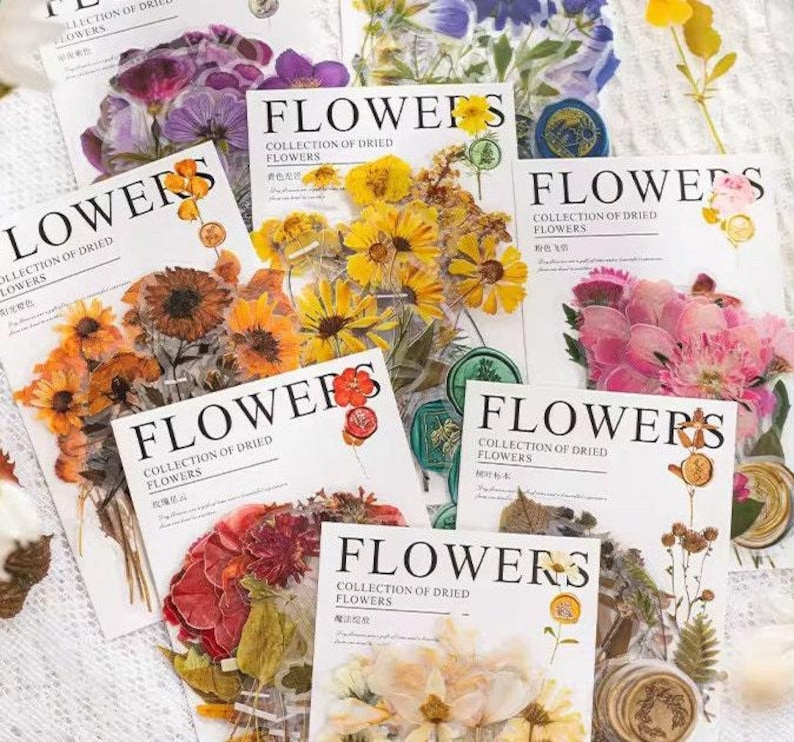 以下が含まれることがあります： 「FLOWERS」の文字が印刷された紙の束で、それぞれにドライフラワーのコレクションが描かれています。花の色は黄色、オレンジ、ピンク、紫など様々です。一部のシートには装飾的なワックスシールが付いています。