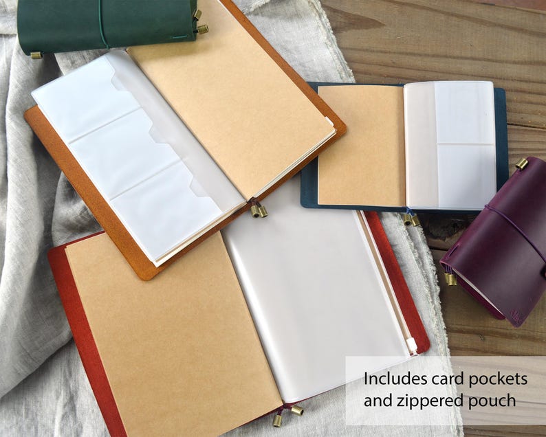 May include: Leather journals in various colors, including green, brown, and burgundy, are displayed open to reveal card pockets and a zippered pouch. The journals have a classic design with a leather cover and a closure.