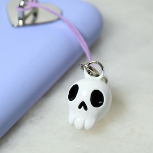 A cute white skull phone charm hangs off of a purple phone case