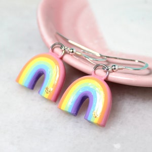 A pair of pastel rainbow earrings with silver fish hook style earring hooks. The earrings are resting against a pink jewelry dish.