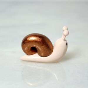 A miniature snail figurine with a sparkly bronze shell sits on a marble surface