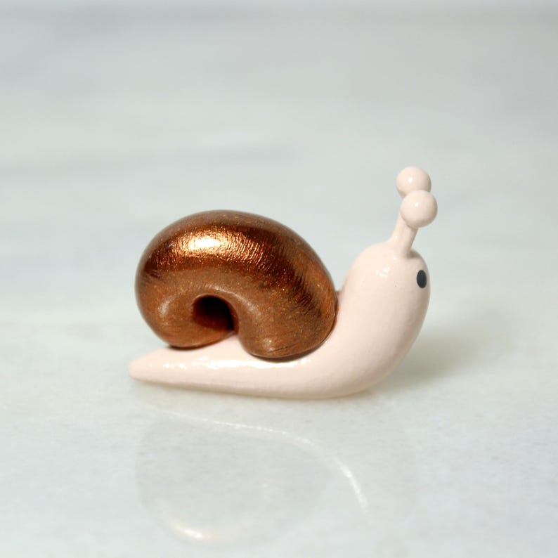 A miniature snail figurine with a sparkly bronze shell sits on a marble surface
