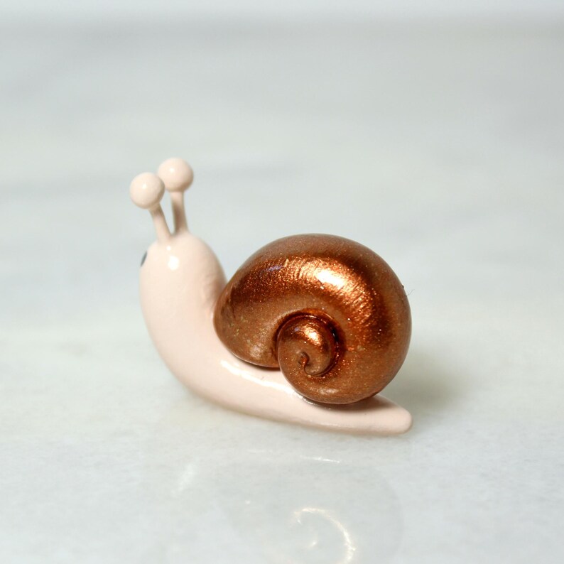 A miniature snail figurine with a sparkly bronze shell sits on a marble surface