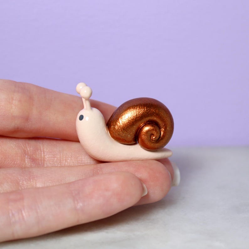 A hand holds a miniature snail figurine with a sparkly bronze swirled shell