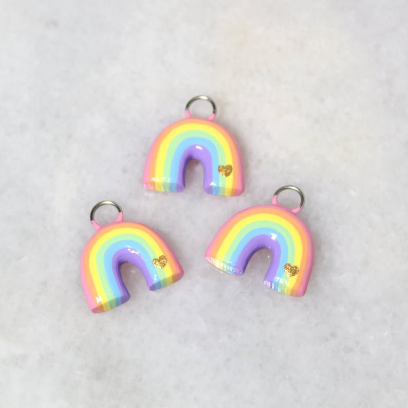 Three pastel rainbow arch charms with tiny gold hearts.