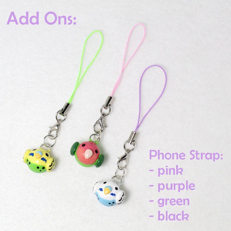 May include: Three colorful phone straps with bird-shaped charms. The charms are yellow, pink, and blue, each with a different design. The straps are green, pink, and purple. Text on the image reads "Add Ons:" and "Phone Strap: - pink - purple - green - black."