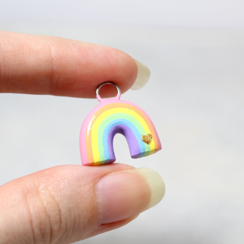 A hand holding a pastel rainbow charm. The charm is about 3/4 of an inch tall.