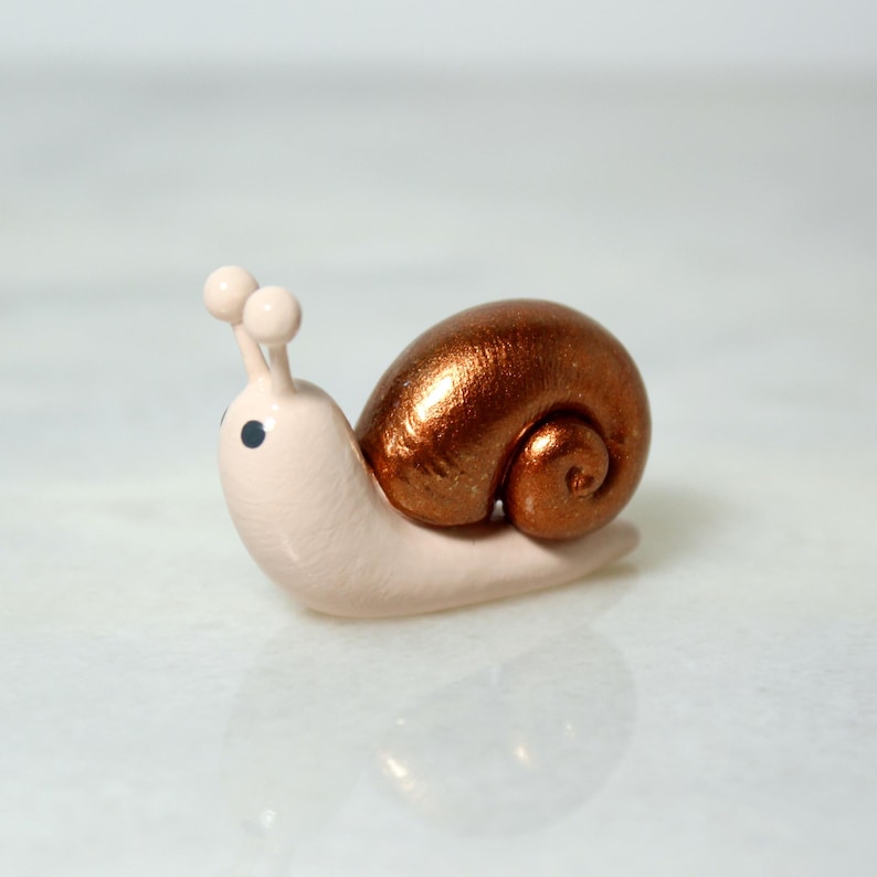 A miniature snail figurine with a sparkly bronze shell sits on a marble surface