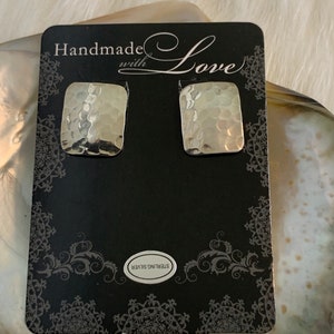 May include: Silver hammered-finish square stud earrings on a black card with the words "Handmade with Love". The card also has a "Sterling Silver" label and decorative border.