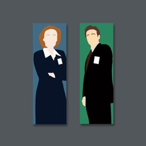 May include: Two figures, a woman with red hair wearing a dark blue suit and a man with brown hair wearing a black suit, stand against a blue and green background. Both figures have white name tags on their chests.