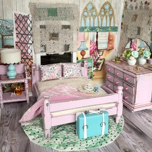 May include: A miniature bedroom scene with a pink bed, nightstand, and dresser. A blue suitcase sits at the foot of the bed. The room has floral wallpaper, a green rug, and decorative artwork.