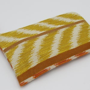 May include: A rectangular zippered pouch with a yellow and cream zigzag pattern. The pouch has a brown border and a decorative wooden bead on the zipper pull. The overall design is a mix of warm colors.