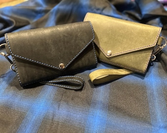 May include: Two leather wallets with blue and purple stitching. The wallets have a flap closure and a strap. The wallets are on a blue and white plaid fabric.