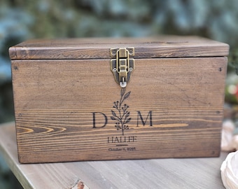 Peut inclure: Une boîte rectangulaire en bois brun foncé avec un couvercle à charnière et un loquet en métal couleur laiton. L'avant présente une gravure laser avec les lettres D et M, un brin floral, le nom HALLEE et la date October 11, 2024.