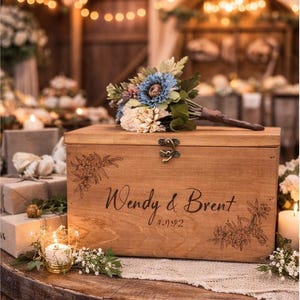 May include: A wooden box with the names "Wendy & Brent" and the date "9-7-92" engraved on the front. The box is decorated with floral designs and a metal clasp. A bouquet of flowers rests on top of the box.
