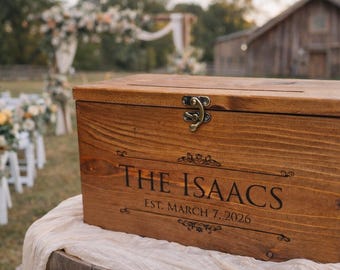 Peut inclure: Une boîte rectangulaire en bois avec un couvercle à charnière et un loquet en métal. L'avant est gravé avec le texte THE ISAACS et EST. MARCH 7, 2026, entouré de fioritures décoratives. Le bois présente une teinte brun moyen.