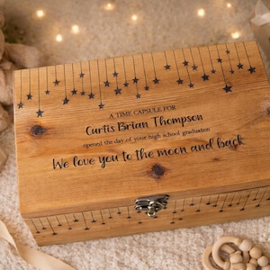 May include: A rectangular wooden box with a metal latch, featuring engraved stars hanging from lines. The text reads: A TIME CAPSULE FOR Curtis Brian Thompson opened the day of your high school graduation We love you to the moon and back.