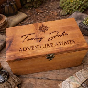 May include: A wooden box with a compass design and the words "Tommy John ADVENTURE AWAITS" engraved on the lid. The box has a metal clasp and is made of light brown wood.