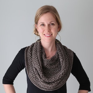 May include: A woman wearing a brown and black knitted infinity scarf with a black long-sleeved shirt.