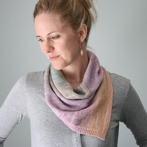 May include: A woman wearing a gray shirt with a multi-colored knitted scarf. The scarf is a gradient of pink, purple, blue, and orange.