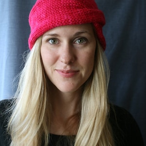 Può includere: Una donna con lunghi capelli biondi indossa un cappello di lana rosa acceso. Il cappello ha un design pieghevole unico ed è realizzato con un filato testurizzato.