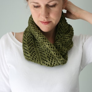 May include: A woman wearing a white shirt with a green crocheted cowl neck scarf.