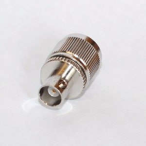 May include: A silver-colored metal connector with a threaded end and a center pin. The connector is designed for electrical connections.