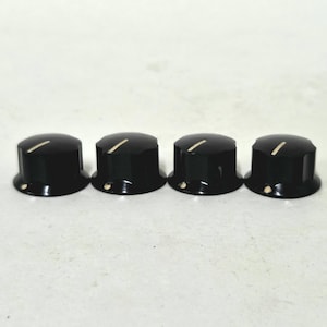May include: A set of four black cylindrical control knobs for electronic equipment. Each knob features a smooth, glossy finish with a single white indicator line on the top surface and a small white dot on the lower side edge.