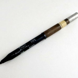 May include: A black and brown pen with a silver tip. The pen has the words "TYPE 5080" printed on the side.
