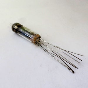 May include: A vintage vacuum tube with a clear glass body and a dark top. The tube has internal components visible through the glass and several metal wire leads extending from the base. The tube is likely an electronic component.