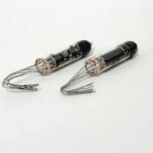 May include: Two vintage vacuum tubes with black tops and clear glass bodies. Each tube has a series of silver wires extending from the base. The tubes are labeled with the text "GE" and "59 U".
