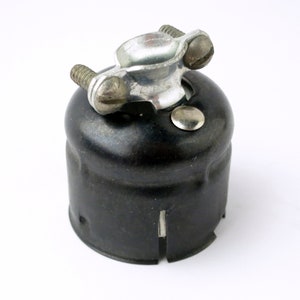 May include: A black metal electrical box with a silver metal clamp on top. The clamp has two screws and a hole for a wire.