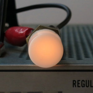 May include: A close-up of a small, round, white light bulb with a brass base. The light bulb is lit and glowing orange.