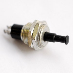 May include: A silver and black push button switch with a black plastic lever. The switch has a threaded base and a small black plastic cap on the end of the lever.