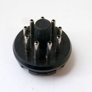 May include: Black plastic circular base with 10 silver metal pins protruding from the top. The base has numbers 1 through 10 printed around the edge.