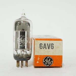 May include: A vintage vacuum tube with a clear glass enclosure and a metal base, next to a small orange and white box. The box is labeled "6AV6" and features a GE logo. The tube has a GE logo on it as well.