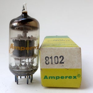 May include: A clear glass vacuum tube with a black top and a yellow label that reads "Amperex". The tube is sitting next to a yellow and green box with the text "Amperex" and "8102" printed on it.