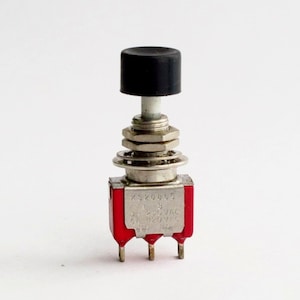 May include: A red push button switch with a black button and silver contacts. The switch is labeled "K3208/3 5 2A 250VAC 5A 120VAC 140 16A".