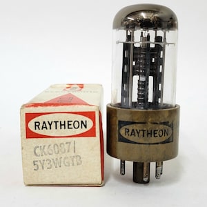 May include: A white ceramic mug with a black handle and the text "But First, Coffee" in a bold, black font. The mug is on a wooden surface. The mug is approximately 10 cm tall.