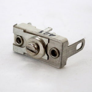 May include: A silver and white ceramic capacitor with a screw on the side and the number "421" printed on it.