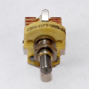 May include: A close-up of a yellow ceramic capacitor with a silver metal top and a label that reads "C804-15PF-MOD-JK".