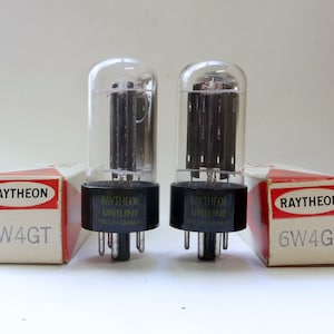 May include: Two vintage Raytheon 6W4GT vacuum tubes in their original boxes. The boxes are white with red accents and the Raytheon logo. The tubes are clear glass with black bases.