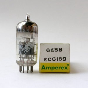 May include: A silver vacuum tube with the text "6ES8 MADE HOLLAND Amperex" printed on the side. The tube is sitting on a white surface next to a yellow box with the text "6ES8 ECC189 Amperex" printed on it.