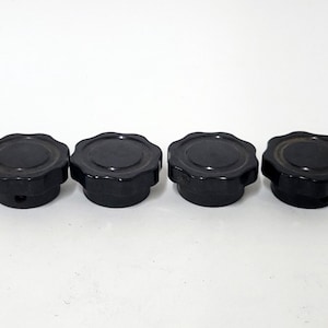 May include: Four black, flower-shaped knobs are arranged in a row. Each knob has a rounded top with a scalloped edge and a cylindrical base. The knobs are made of a glossy, dark material.