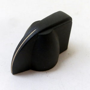 May include: Black plastic knob with a gold line down the center. The knob is shaped like a teardrop with a flat top.