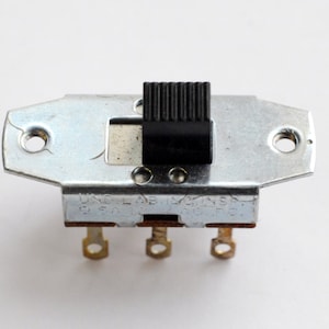 May include: A silver toggle switch with a black knob and three terminals. The switch is labeled "UND. LAB. INSP. 60 SA - AC ONLY".
