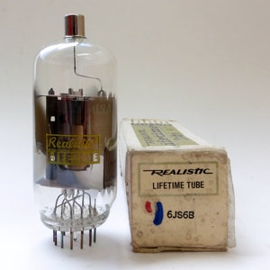 May include: A vintage Realistic Lifetime Tube with a clear glass bulb and a silver cap, next to its original box. The box is off-white with the text "Realistic Lifetime Tube" and "6JS6B". The tube has a gold label.
