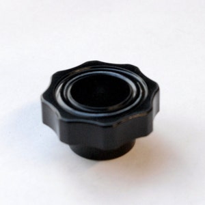 May include: A black plastic knob with a star-shaped design and a raised center. The knob has a smooth, matte finish.