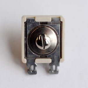 May include: A white ceramic electrical outlet with a silver metal screw in the center.