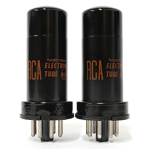 May include: Two black RCA Radiotron Electron Tube vacuum tubes. The tubes have a cylindrical shape with a base containing pins. The RCA logo and "Electron Tube" are printed in orange on the tubes. Made in the USA.